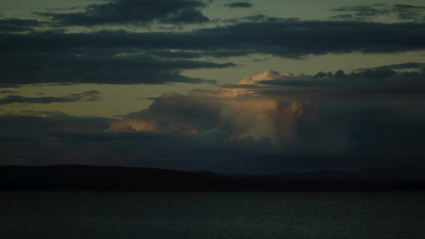 Evening light reflects on dense clouds above a calm lake