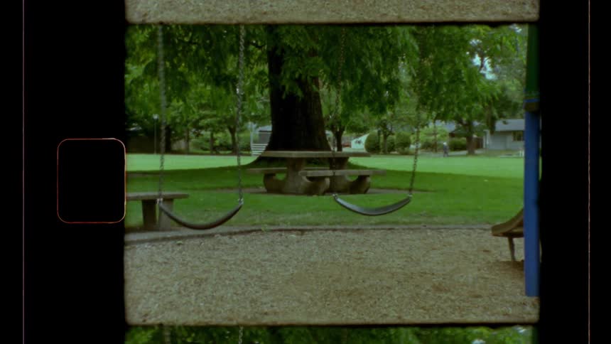 Two empty swings sway back and forth in a park while a runner runs in the distance during the daytime