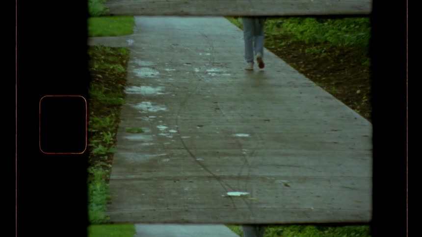 The legs of a person wearing jeans walking on a concrete pavement