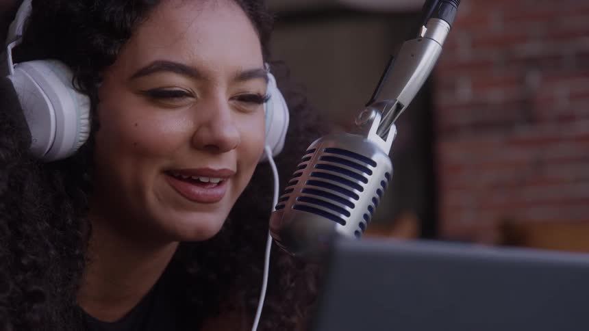 Female performer uses a large metal microphone and headphones while looking at a laptop