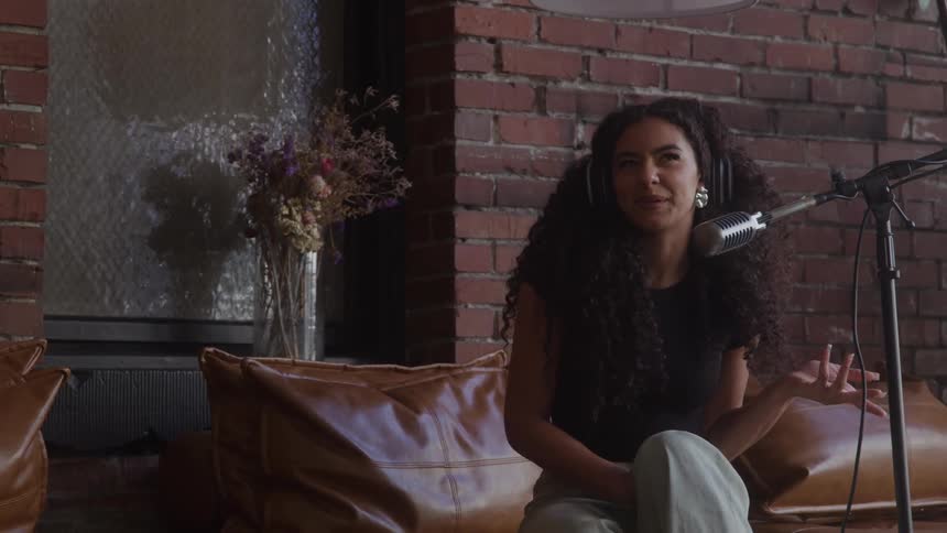 The woman is sitting on the couch talking into a microphone