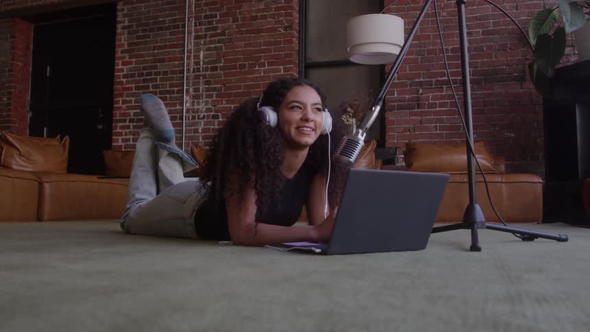 The woman lays in front of her laptop and talks into a microphone