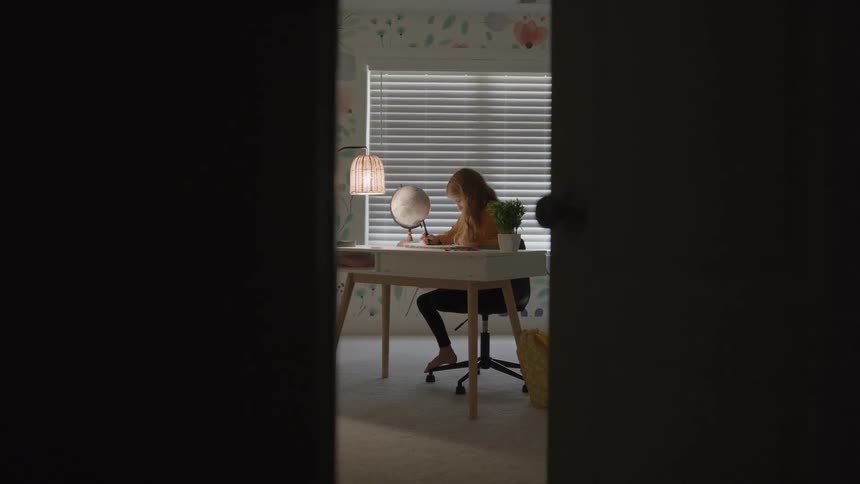 Teenager stops writing to think while sitting at a desk at home