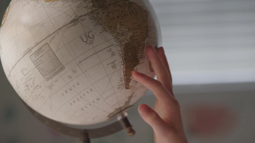 A young girl uses her had to slowly rotate a globe model of earth
