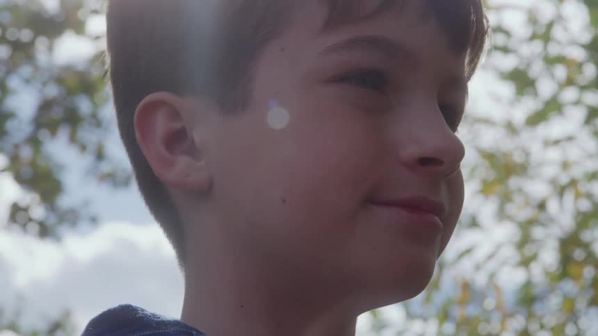 Boy smiles slightly while standing under the trees on a sunny autumn day