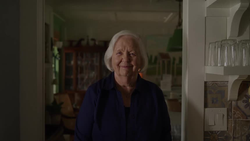 The face of a whitehaired lady standing in a room and starting to smile