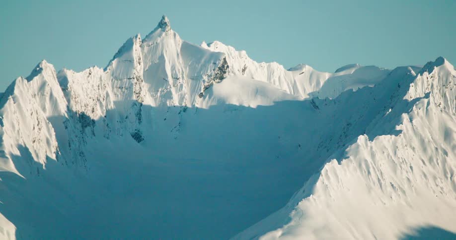 Shadows fill the narrow valleys between snow covered mountains on a winter day
