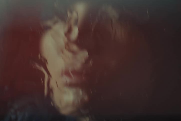 A distorted face appears through blurry glass in darkness