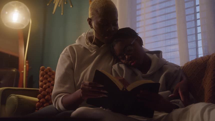Mother and daughter cuddle on the sofa while reading a book together