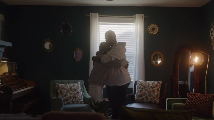 Mother and daughter hug in their living room while partially silhouetted by a window