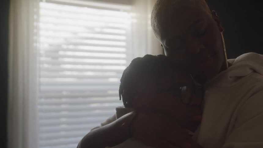 Mother and son remain embraced under the gentle light streaming through the window
