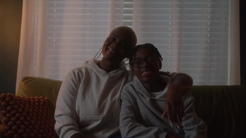 Mother and son smile while sitting together on the couch in soft window light