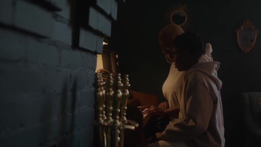 Mother and son play piano under warm light in a dimly lit room