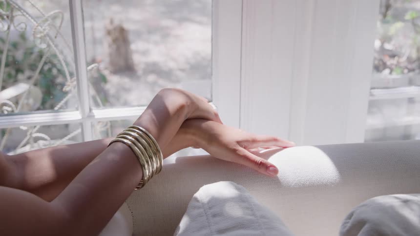 Closeup of a womans hands resting on a couch by a sunlit window