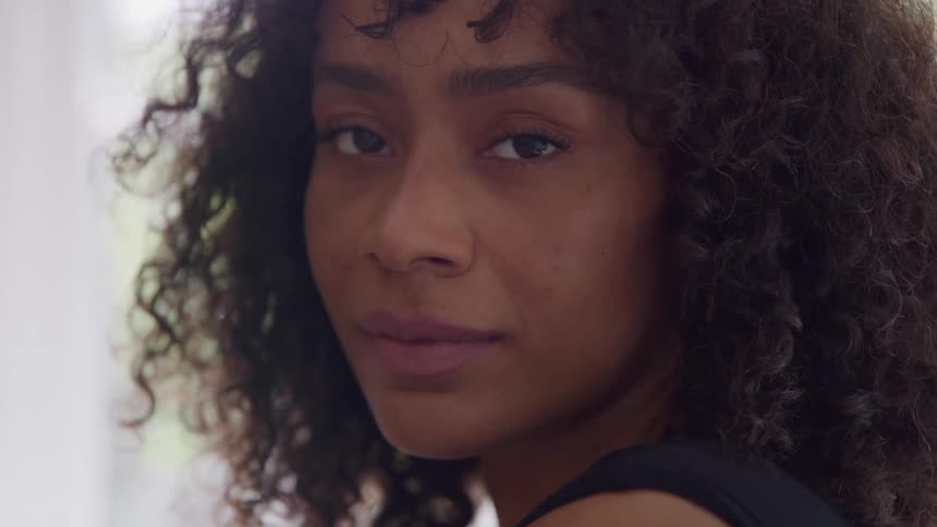 Closeup of a woman with curly hair and eyes closed appearing calm and content as she savors a quiet moment