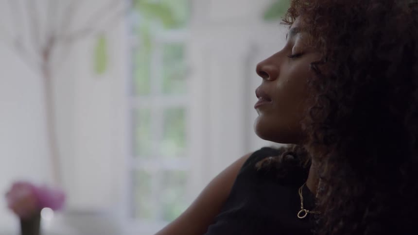 Woman with curly hair leans her head back while sitting in a sunny room
