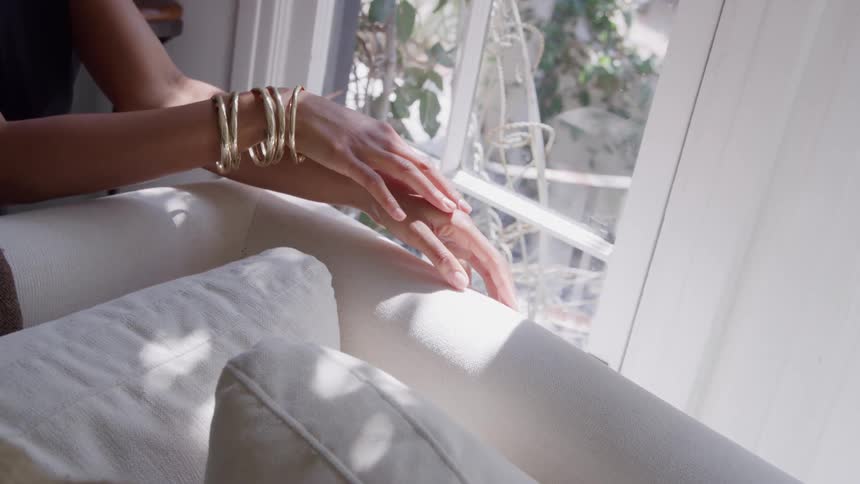 Hand with golden bracelets rests on the arm of the couch near the window