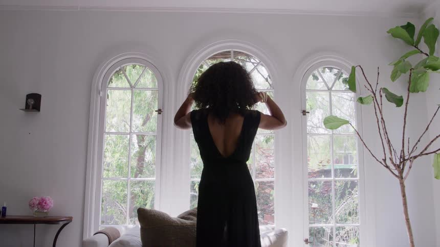 The woman reaches up and brushes her hair back by the window