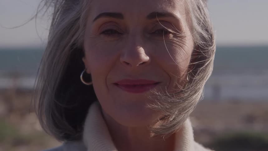 Woman smiles on a beach as the wind blows her hair under bright sunlight