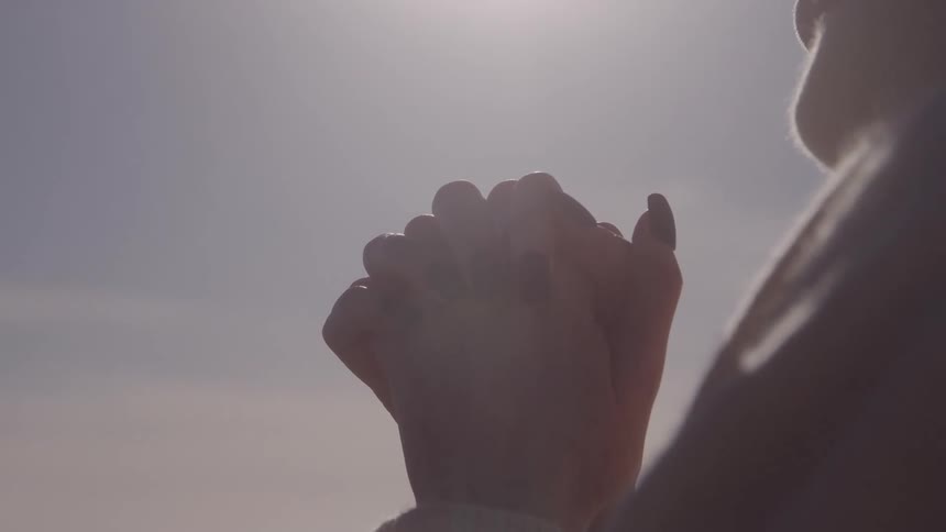Clasped hands rise under the gentle sunlight