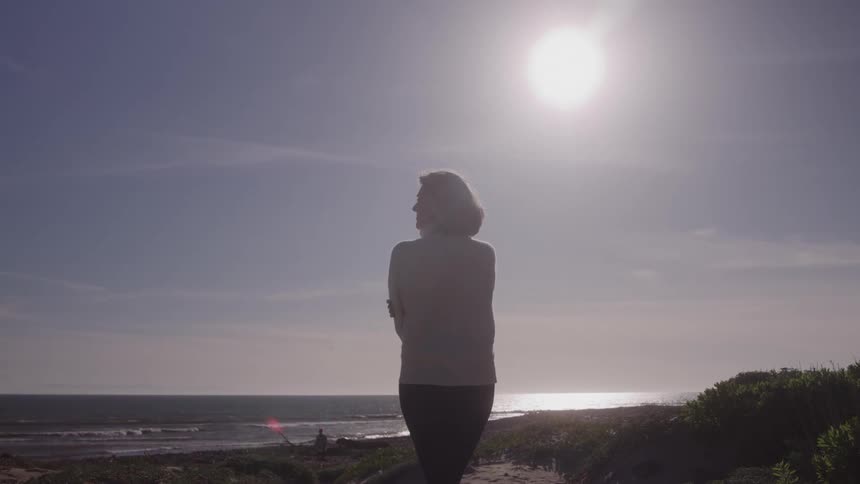 Woman walks on the beach under the sun surrounded by light and tranquility