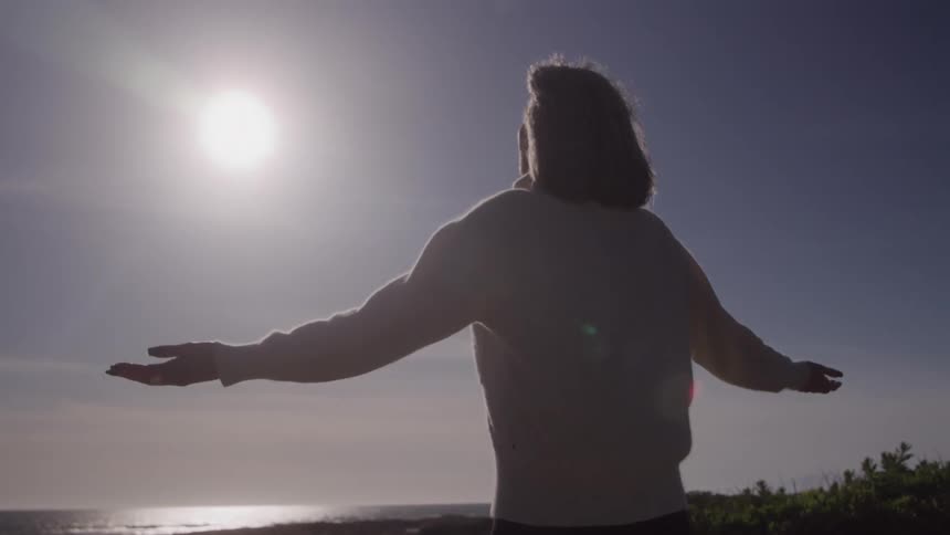 Woman with open arms facing the sea embracing the sunlight