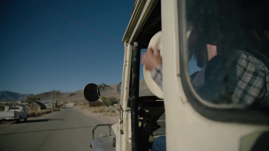 A man waves out the door of a moving vehicle