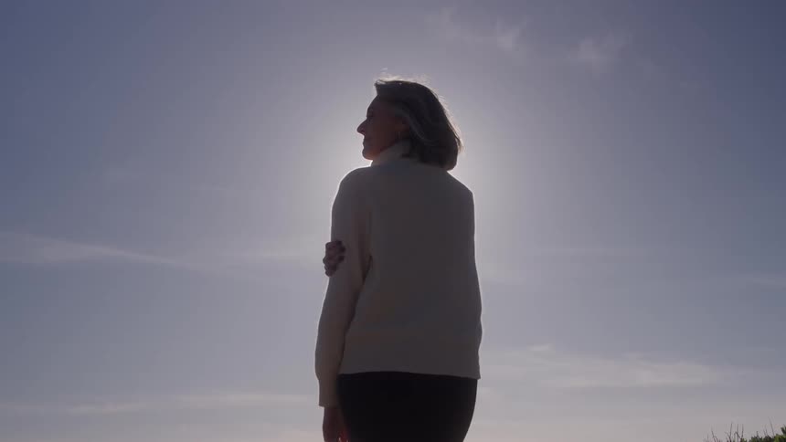Woman in a light sweater is illuminated by the sun while looking at the sky
