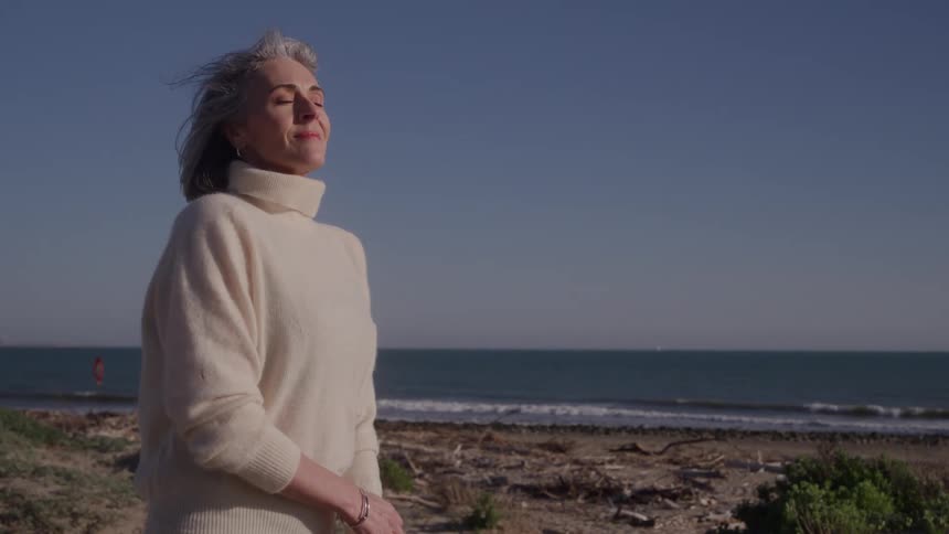 Woman in a light sweater enjoys the sea breeze under the blue sky