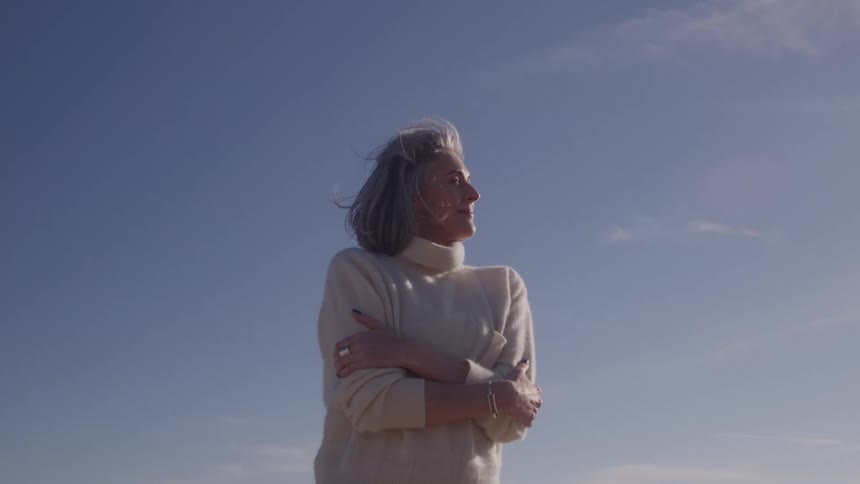 Woman stands outdoors with arms crossed under bright sunlight