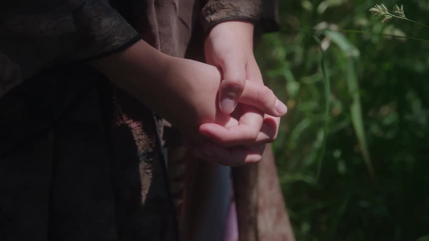 Clasped hands rest among leaves and natural light