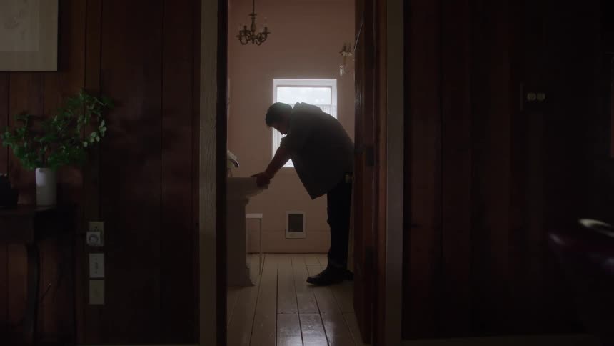 Man leans over the sink in a bathroom lit by natural light