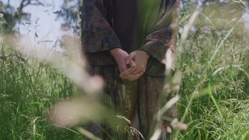 Person keeps their hands clasped among tall grass under sunlight