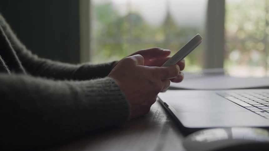 Person holds a smartphone in front of a laptop on the desk