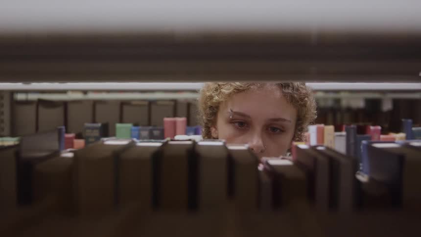 A young student concentrates on selecting a book from a library shelf