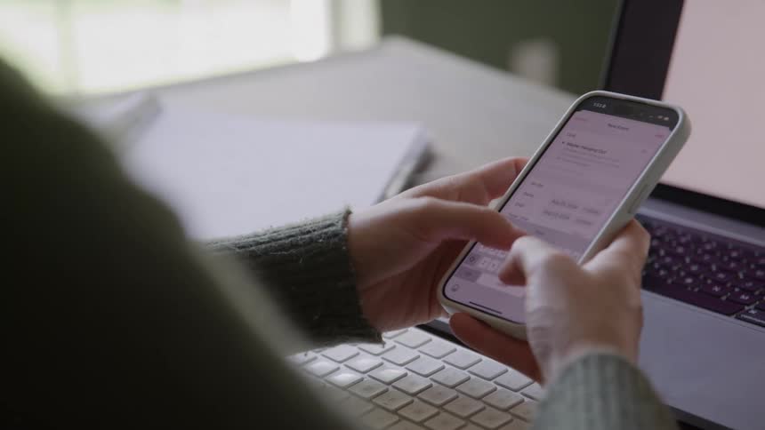 A person scrolls on a smartphone at a desk in a modern office