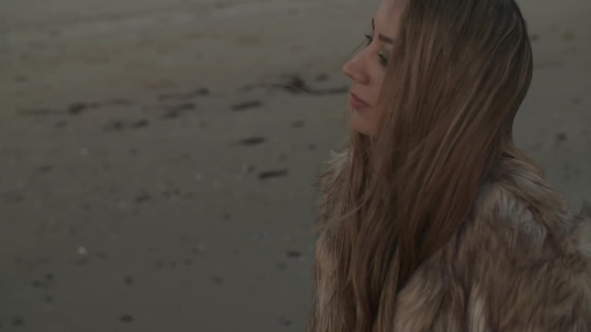 Woman wearing a fur jacket standing on a beach
