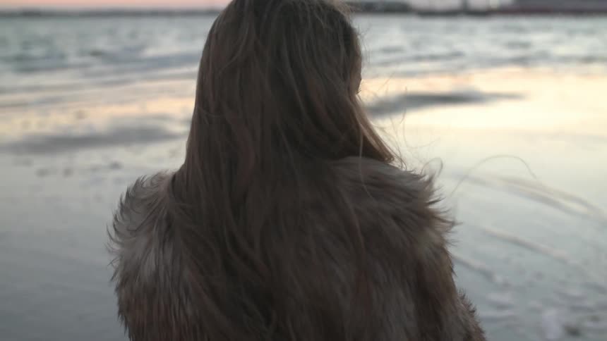 Woman standing by the water as the sun sets