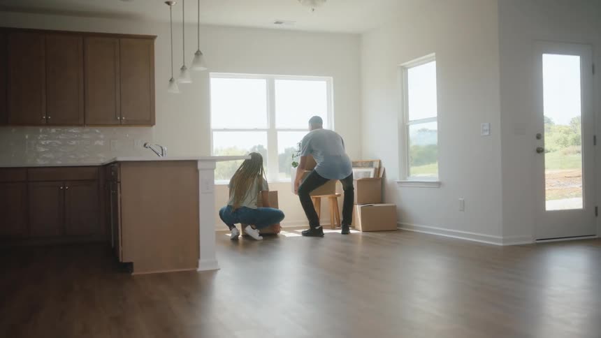 The man and woman carry cardboard boxes into the room