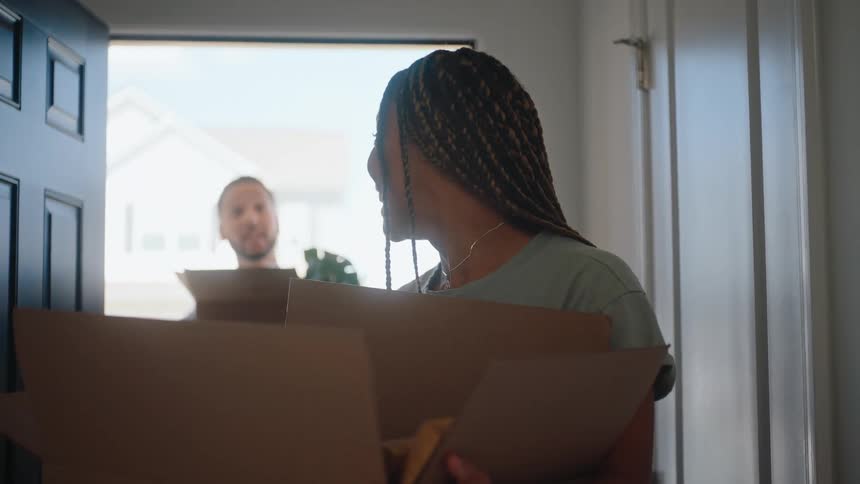The couple are carrying cardboard boxes into the home as they move in