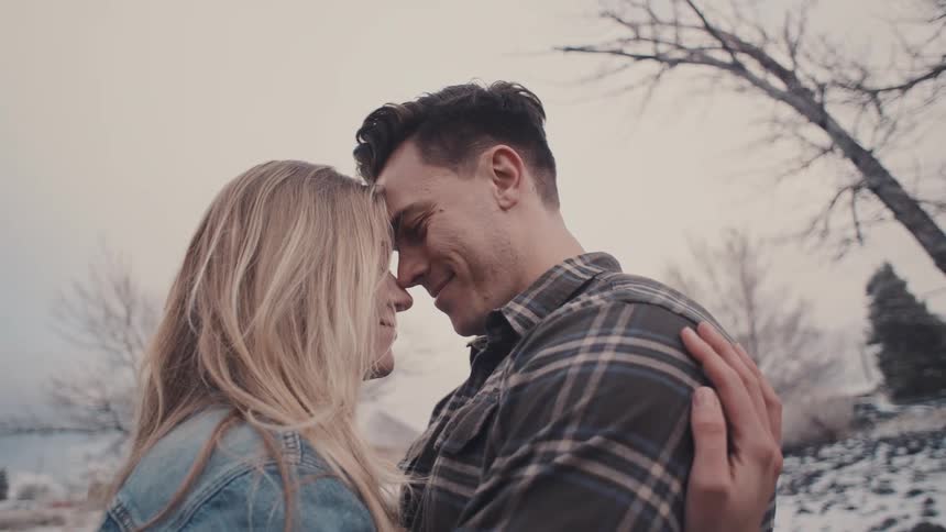 A man and woman touch noses and smile on a snow covered street
