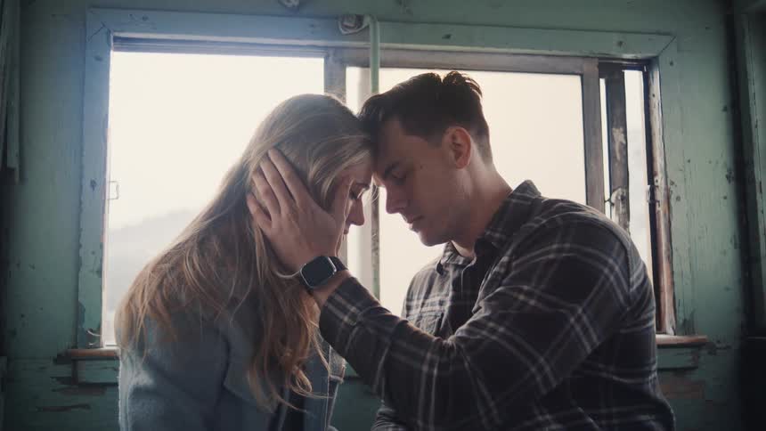 A young couple sits in a train car touching foreheads tenderly