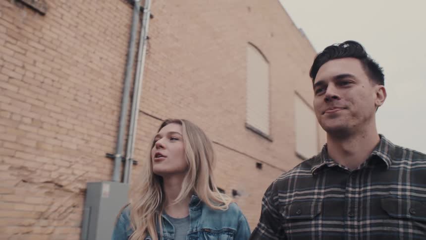 A couple walks hand in hand down the middle of the street at midday holding each other close and laughing as they enjoy a joyful moment together