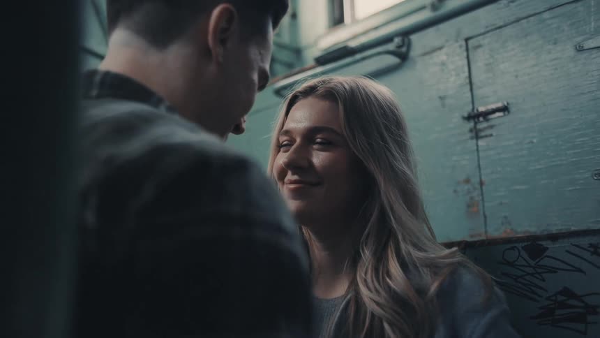 The video is a closeup shot of a young couple standing inside what looks like a metal train car or industrial area they are touching foreheads in an intimate embrace suggesting a moment of comfort or affection in a rugged setting
