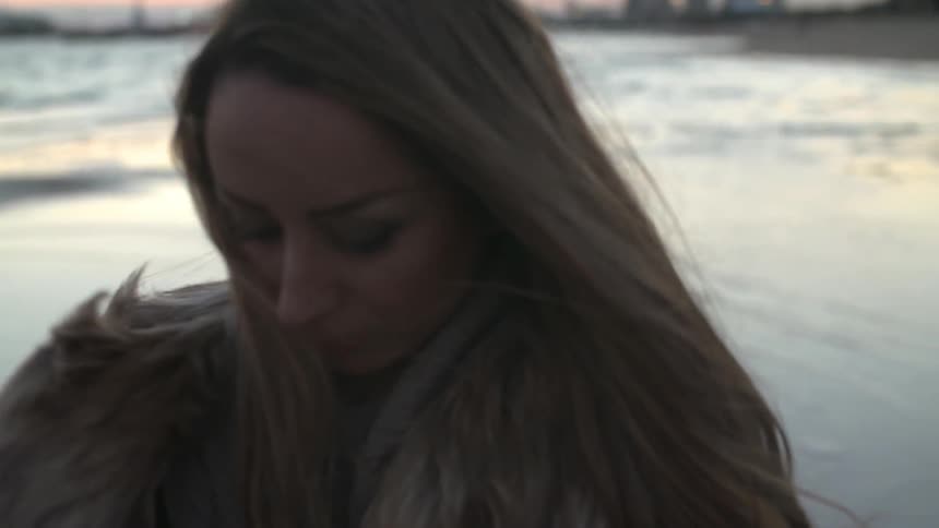 Woman walks down a beach in a fur coat
