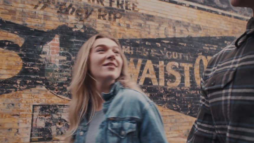 A couple holding hands walks by an old building in a city