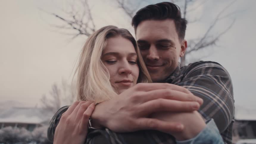 Close up of a young couple hugging each other while standing outdoors during daytime