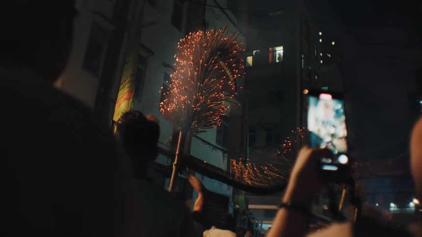 People raise flaming structures during a nighttime parade on a busy street