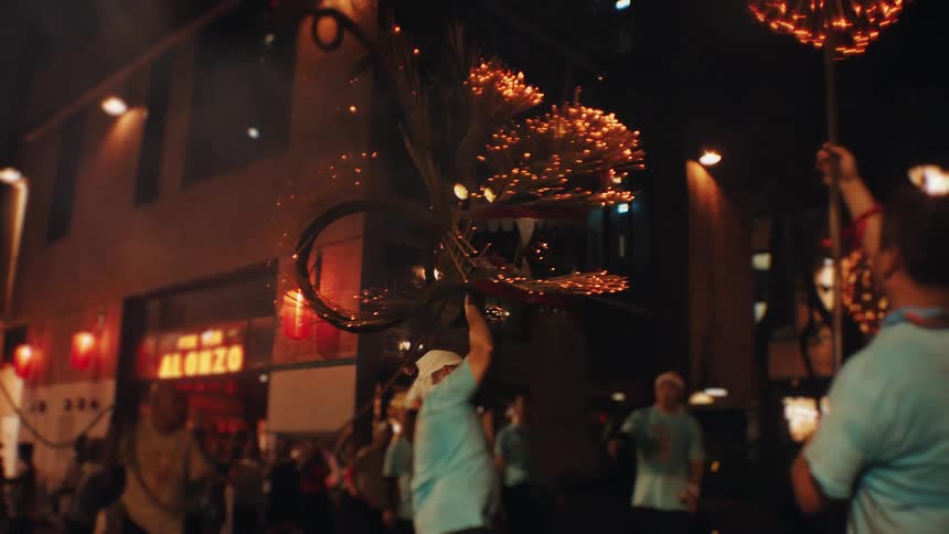 People take part in a nighttime celebration with flaming sticks surrounded by lights and spectators