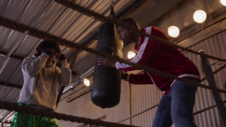 Coach motivates young boxer during an intense punching bag session
